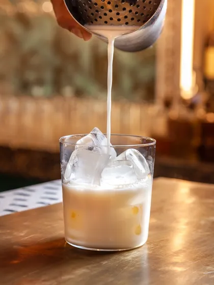Crafting our Lemongrass Pina Colada. We start by pouring our house-made mix of lemongrass-infused rum and roasted almond orgeat over ice.