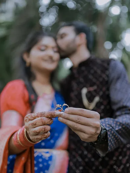 A creative engagement ring shot that tells a story. The couple holds their rings in the foreground, symbolizing their promise, while they share a loving moment blurred softly in the background.