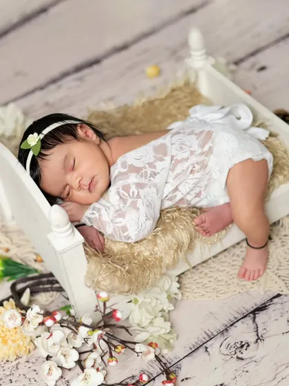 A sweet baby girl sleeping peacefully on a tiny wooden bed. We use delicate lace outfits and props to create timeless and classic newborn portraits.