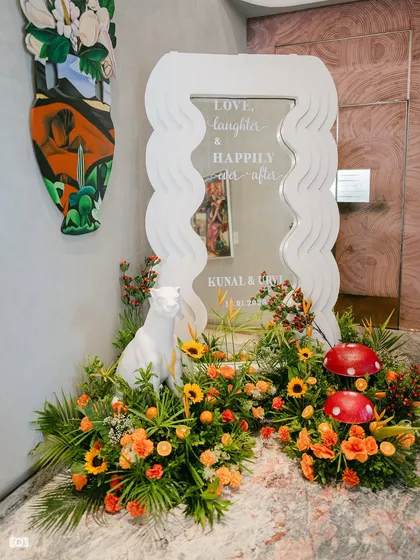 A personalized welcome mirror with a modern wavy frame, surrounded by sunflowers, tropical leaves, and quirky animal and mushroom props.