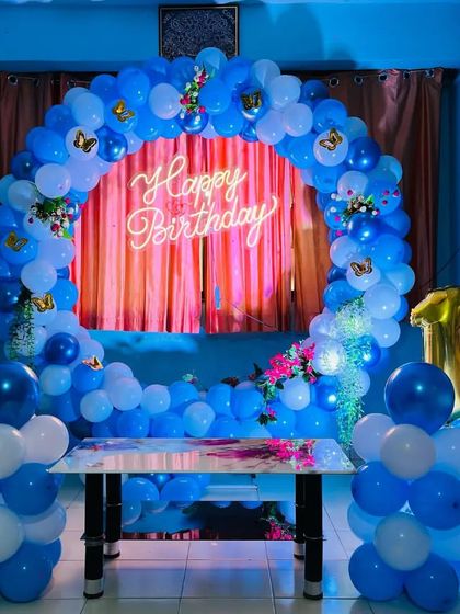 A beautiful first birthday setup in blue and white, with butterfly accents, a neon sign, and a large number '1' balloon.