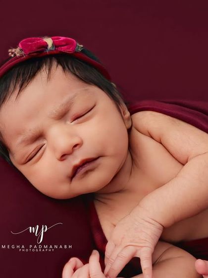 A beautiful portrait of a sleeping baby girl wearing a delicate red headband, wrapped in a matching swaddle.