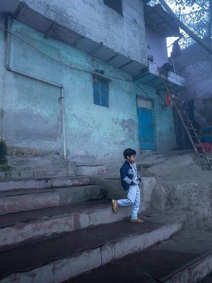 A young boy descends the steps of the ghat on a foggy morning, a slice of daily life captured in the ethereal mist.