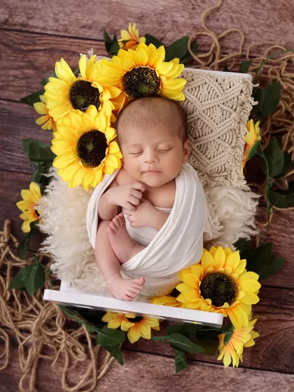 Bright and cheerful, this newborn is surrounded by sunny yellow sunflowers. The rustic wood background and natural textures create a warm, earthy feel for this baby boy photoshoot.