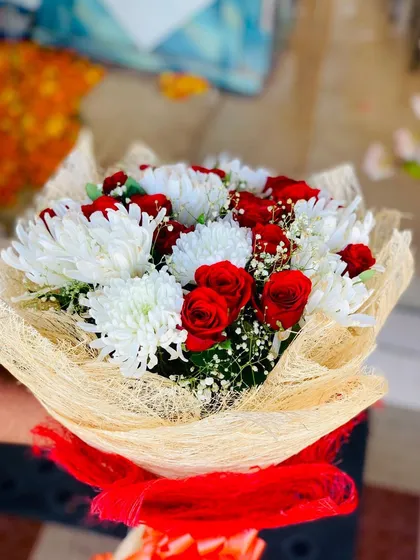 A bouquet of red roses and white chrysanthemums wrapped in natural jute netting. The red ribbon provides a bright pop of color against the neutral wrapping.