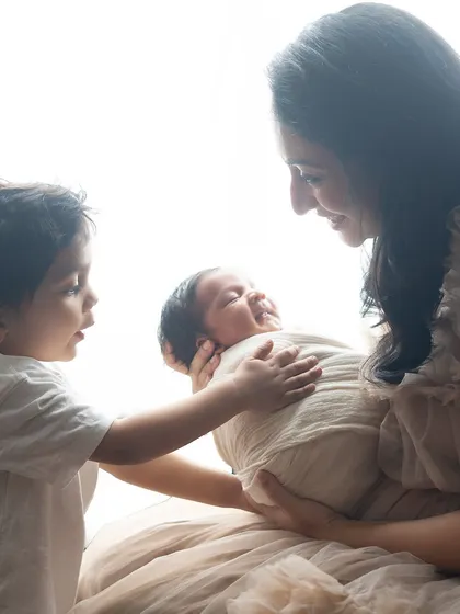 A big brother gives his newborn sibling a gentle touch. The high-key lighting creates a soft, dreamy effect that enhances the sweetness of the moment.