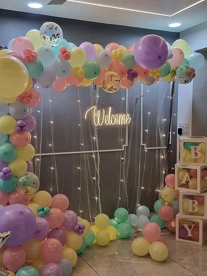A full view of the pastel balloon arch against a grey wall with a sheer curtain and fairy lights. This setup is versatile and can fit in many different home spaces.