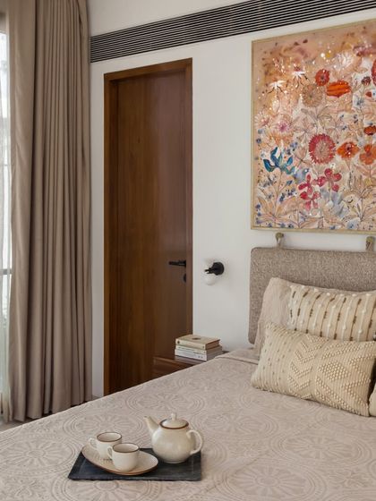 The master bedroom in the House of Terraces features a stunning, large-scale floral artwork that acts as a headboard. The neutral, textured bedding and warm wood tones create a luxurious and inviting atmosphere.