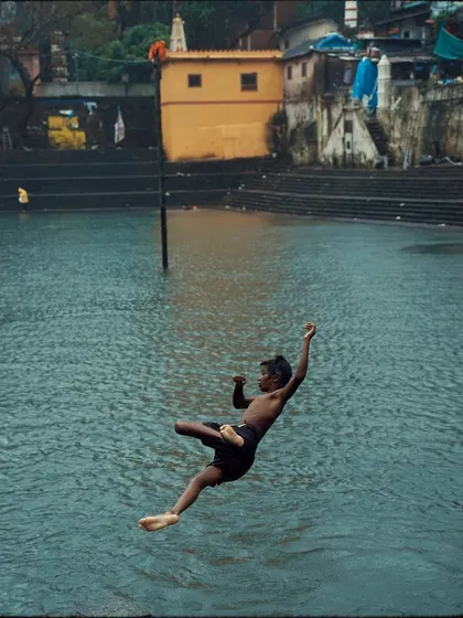 A boy joyfully leaps into the water at Banganga Tank. This perfectly timed action shot captures a moment of pure freedom and energy, a common sight during the monsoons here.