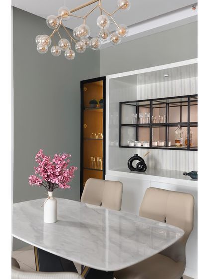 A closer look at a sophisticated dining setup. The combination of a white marble table, a modern bubble chandelier, and a sleek, built-in bar unit with internal lighting creates an atmosphere of refined luxury.