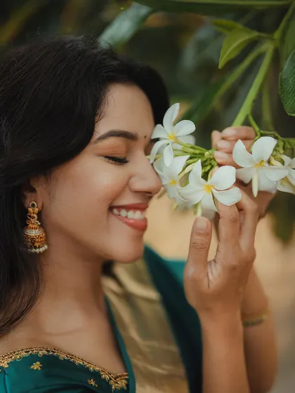 A sweet and joyful shot of Mirnalini smelling fresh flowers. Her bright smile and the natural lighting make this a beautiful, candid moment.