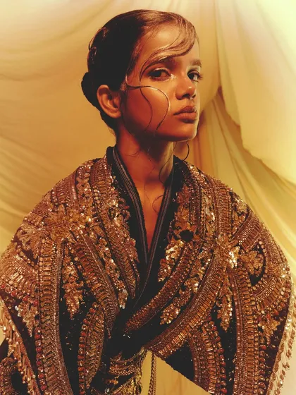 An avant-garde look featuring intricate gold embroidery and sleek, graphic hair, paired with a shimmering gold eye.
