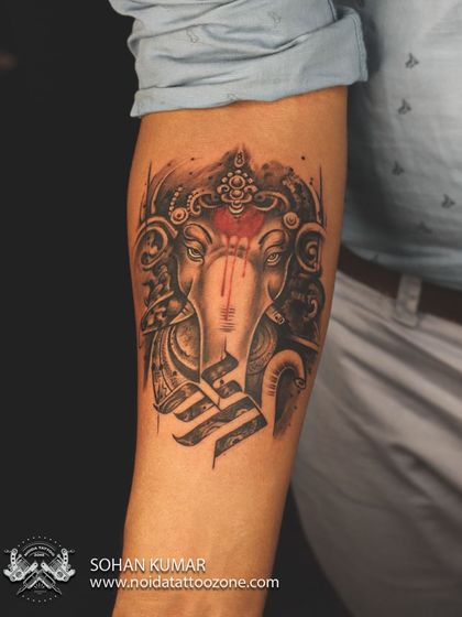 A finished look at our Lord Ganesha tattoo with a Swastika. The design uses abstract and realistic elements, with a bold red tilak that makes the black and grey work pop.