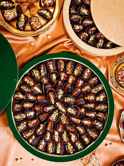 A luxurious flatlay of premium dates arranged in ornate green gift boxes. The rich colors and textures of the silk background and dates create an opulent and festive feel.