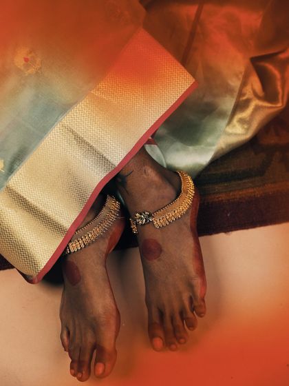 A detail-oriented shot focusing on traditional elements. The alta on the feet and the classic gold anklets are styled with a beautiful silk saree, telling a story of heritage and artistry from head to toe.