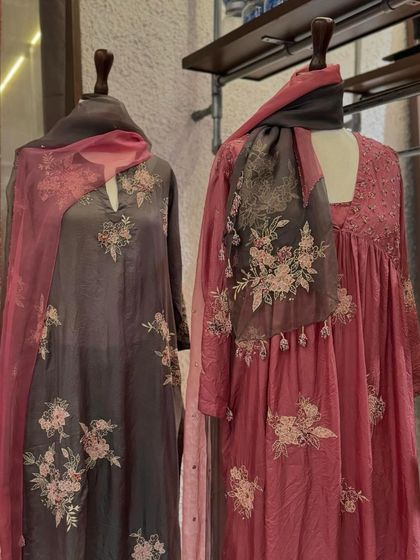Two elegant suits from Kora's collection, featuring delicate floral embroidery on a grey and pink color palette.