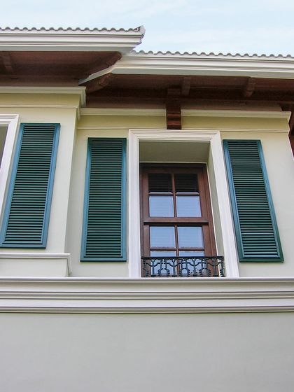 A close-up of the facade detailing, showing the contrast between the dark green shutters, the wooden window frames, and the crisp white moldings under the eaves.