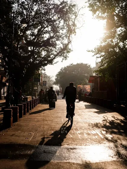 The early morning sun casts long shadows as a lone cyclist pedals through the quiet streets of Old Delhi. This is the magical time before the city fully awakens.
