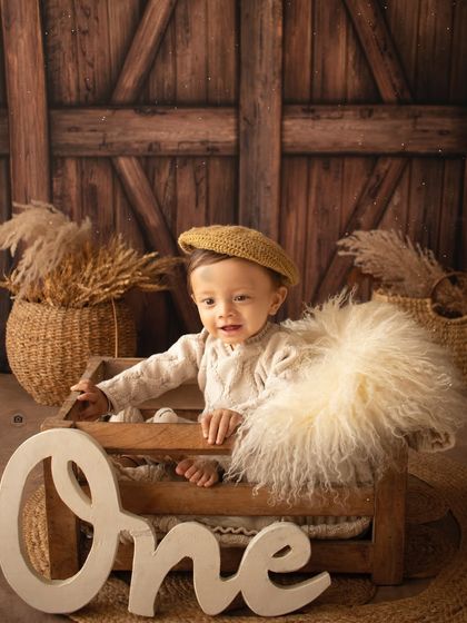 A happy one-year-old in a rustic wooden crate, part of our popular woodland theme. The "One" sign marks his special milestone.