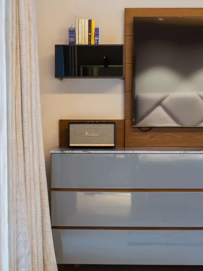 A detail of the custom TV console at Rue 32, finished in a sleek grey lacquer with wood accents. This piece combines closed storage to hide clutter with open surfaces for essentials like a speaker, blending aesthetics with everyday practicality.