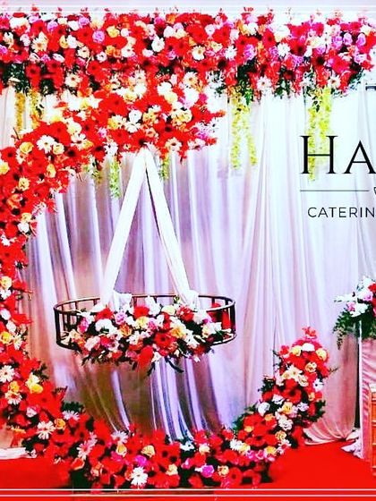 A striking naming ceremony setup with a cradle decorated in bold red flowers. The crescent moon frame and white curtain backdrop create a dramatic and elegant look.