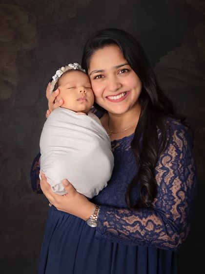 A glowing new mother holding her peacefully sleeping newborn. The simple swaddle and dark backdrop put all the focus on the beautiful bond between mother and child.