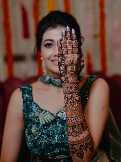 A smiling bride peeking from behind her hand, giving a great view of the personalized initial 'S' on her palm.