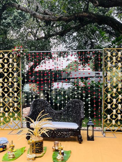 An elegant outdoor setup for an engagement or pre-wedding event. The decor features a backdrop of hanging flower strings and ornate black seating, creating a sophisticated look.