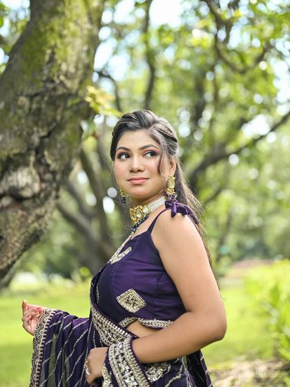 An outdoor portrait of the model in the purple lehenga, with the green background making the rich color pop.