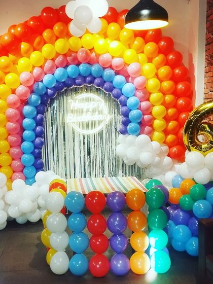 A massive rainbow balloon backdrop for a big celebration. This setup includes a cake table made of balloons and creates a very colorful and impressive photo stage.