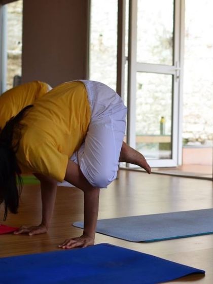 A student practices Kakasana (Crow Pose) in our sunlit yoga hall, a foundational arm balance for more advanced postures.