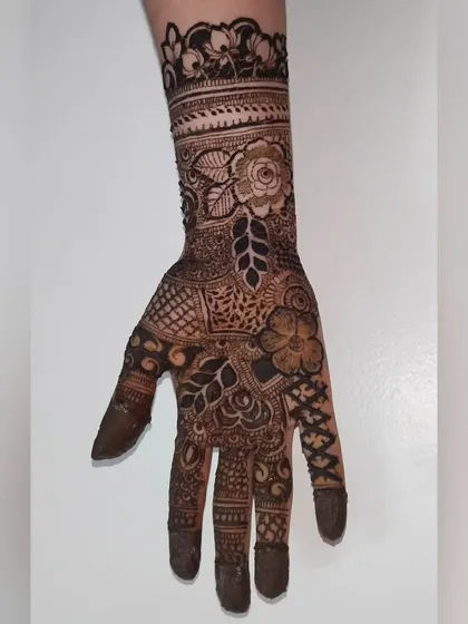 A classic bridal design for the back of the hand, featuring a large central flower connected to detailed finger patterns and a wrist cuff.
