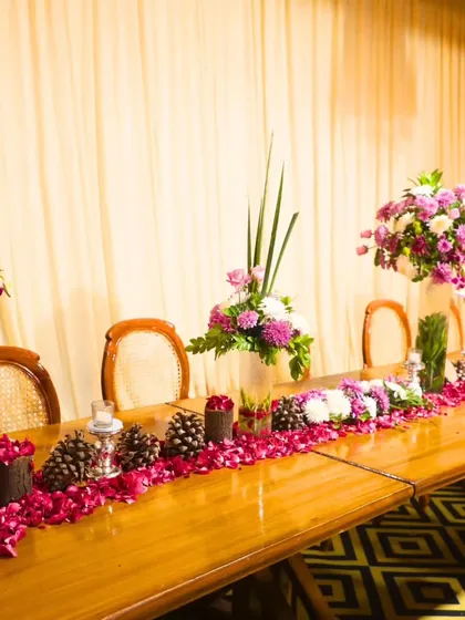 A close-up of a beautifully decorated head table, adorned with rose petals, pinecones, and floral arrangements. We excel in creating memorable moments with our attention to detail.