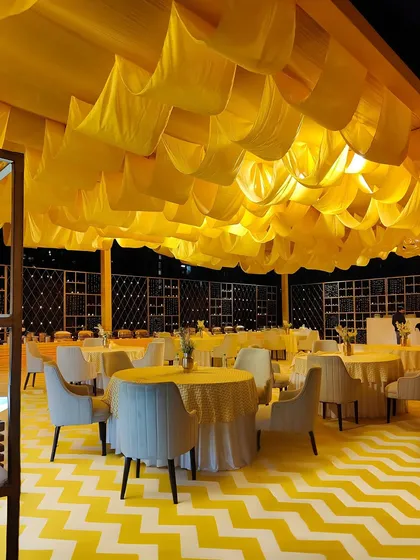 An outdoor dining area with a yellow and white chevron floor and a ceiling of draped yellow fabric. This cohesive design creates a vibrant and cheerful atmosphere for guests.