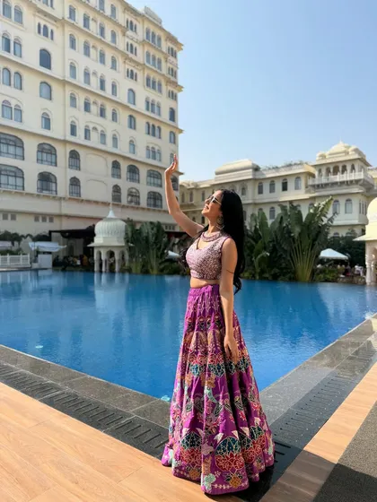 Posing by the pool in my purple lehenga at a beautiful hotel. The grand architecture provides a stunning backdrop.