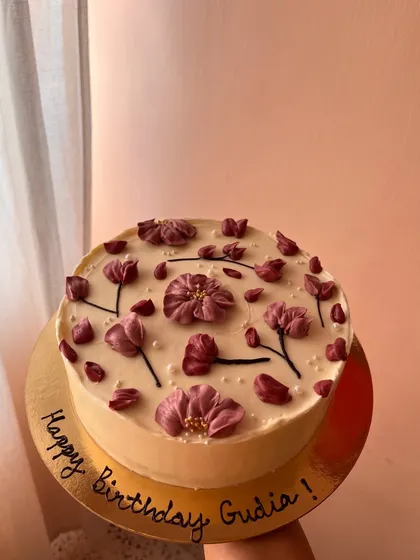 A sophisticated floral cake with hand-piped purple flowers and petals scattered across a smooth buttercream surface.