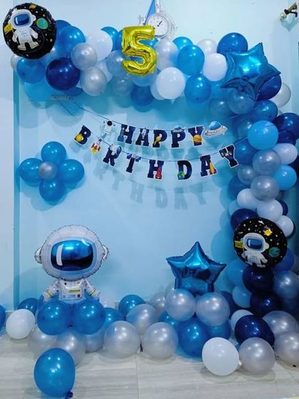 A simple space-themed decoration for a 5th birthday with an astronaut foil balloon and a blue and silver balloon arch.