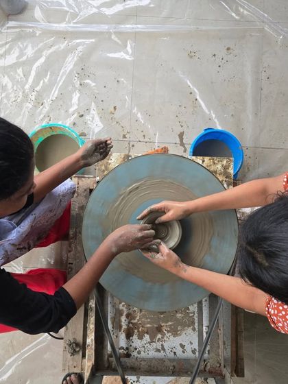 An overhead view of two people working together on the wheel. This perspective shows the symmetry and motion involved in creating a piece from clay.