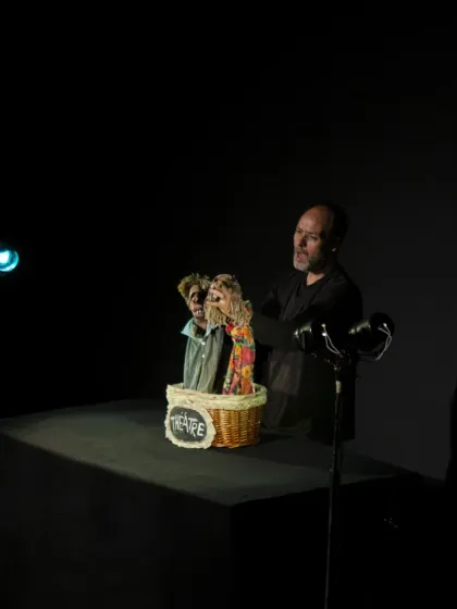 The puppeteer of 'Life (VIDA)' interacts with two of his hand-puppet creations. His expressive face mirrors the emotions of the story he is telling.