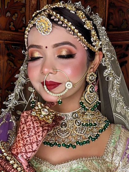 A bride wearing a green and gold Kundan set with a matching nath and maang tikka. The detailed craftsmanship of the choker makes it a standout piece.