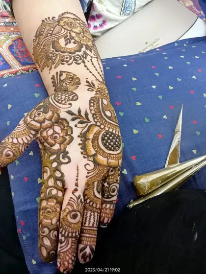 A close-up of a fusion design being applied. You can see the henna cone I use to draw the fine lines of the peacock and floral elements.
