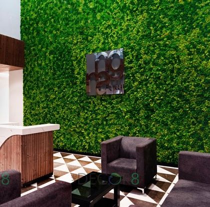 A full-height moss wall creates a dramatic backdrop for this reception area. The vibrant green contrasts beautifully with the modern desk and geometric floor, making a powerful first impression on visitors.