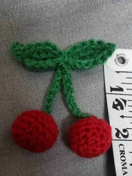 A close-up of my cute little cherry keychain, fresh off the hook. The measuring tape shows its small, delicate size, perfect for adding to your keys or bag.