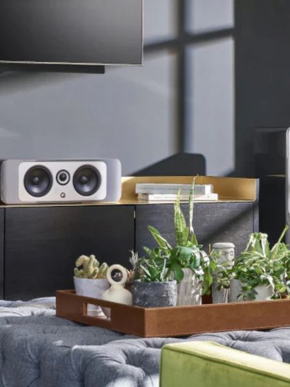 This stylish living room features a Q Acoustics setup, including a center channel speaker on the console and a floor-standing tower speaker. It shows how high-performance audio can be integrated into a beautifully decorated space with plants and modern furniture.