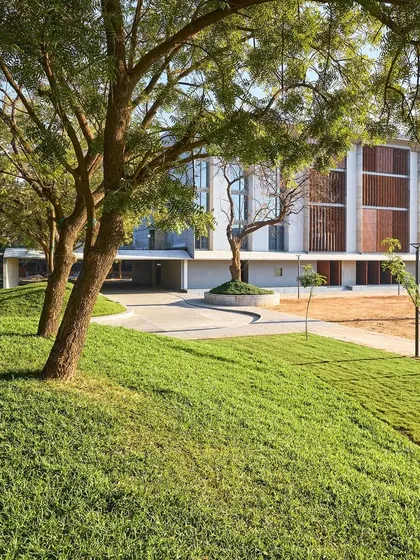 The landscape design for the JSW School of Public Policy at IIM Ahmedabad incorporates gentle mounds and preserved trees. This creates a soft, natural foreground that contrasts with the building's clean architectural lines.