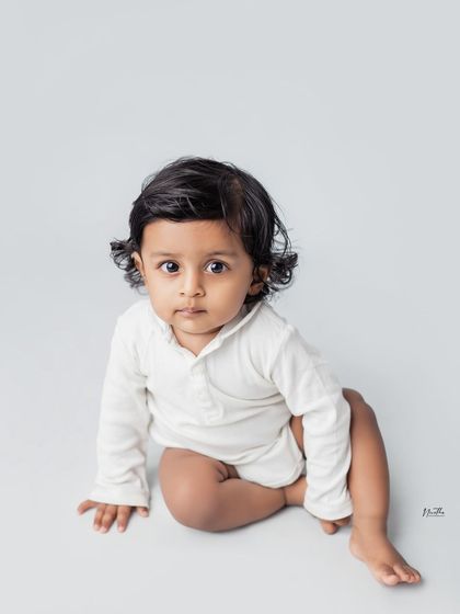 A simple portrait of a baby boy sitting on a grey background.