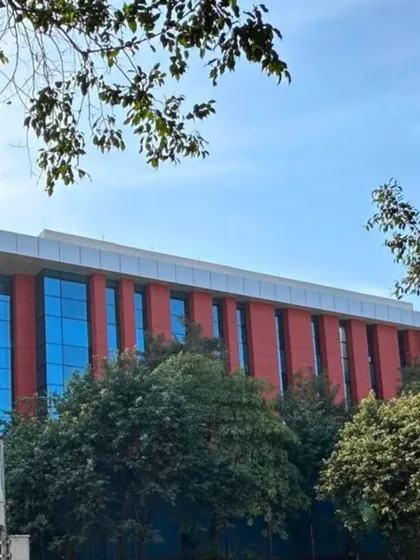 A view of a modern school building we designed, seen through the trees. The facade combines red panels with vertical blue glass sections, demonstrating a contemporary approach to educational architecture.
