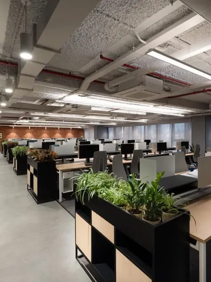 A view across a large open-plan office, showing the use of planters on storage units to add greenery and act as natural space dividers. The exposed ceiling and brick wall add an industrial touch.
