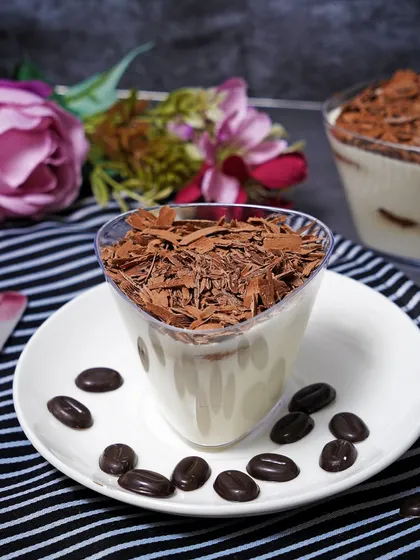 A dessert cup filled with tiramisu and topped with chocolate shavings. This photograph highlights the delicate layers and textures of a classic Italian dessert.