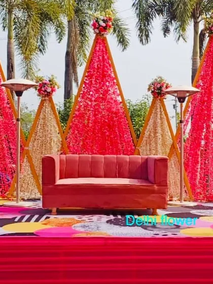 A modern Haldi stage design with geometric, cone-shaped backdrops made of red and gold flowers, set against a quirky, colorful floor.